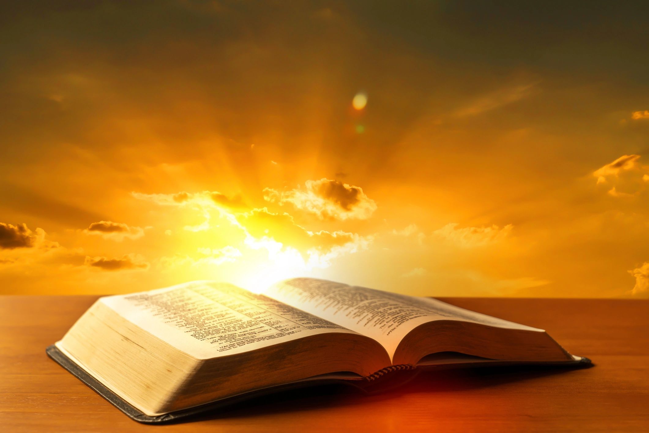 Open Bible on a wooden desk with warm light