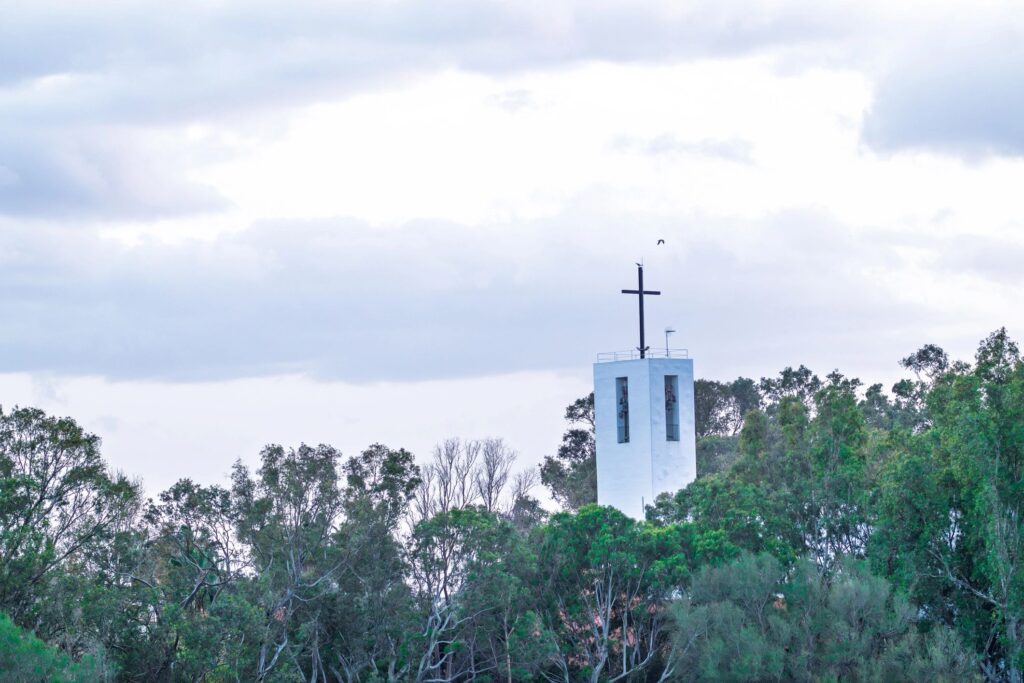 Church steeple and cross rising above forest trees